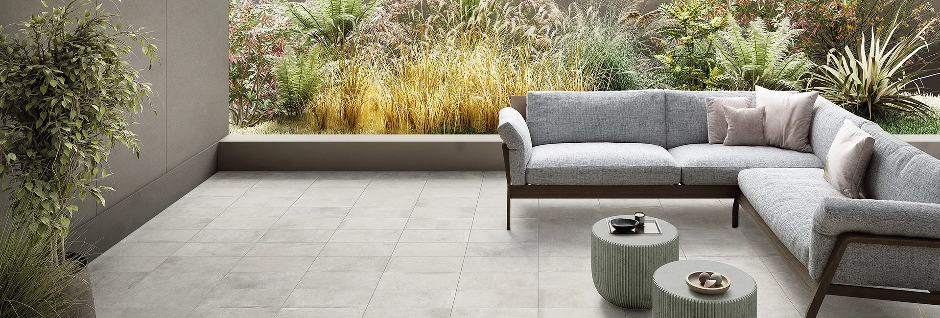 Italian: "Pavimento in gres effetto cemento collezione Street colore Milano Silver in terrazza con divano e giardino.