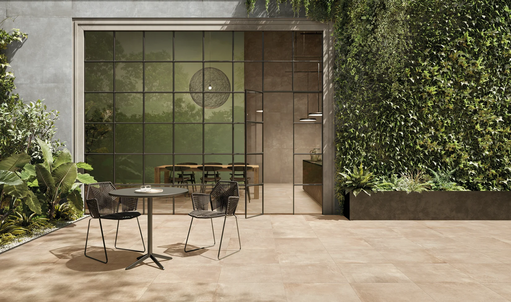 Terrazza esterna con piastrelle 60x60, effetto cemento della collezione Noord colore Gold, arredata con sedie moderne e viste su un giardino verticale lussureggiante.