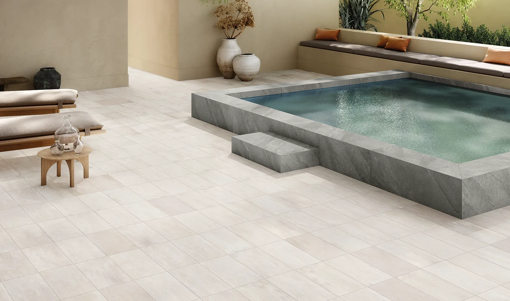 Milano Ivory cement-effect porcelain stoneware floor from the Street collection, laid in a chic outdoor space by a modern pool with dark stone steps and stylish garden furniture.